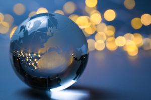 A glass globe sits on a dark grey surface; in the distance, out of focus lights glimmer; these are reflected as pinpricks of light within the glass globe.