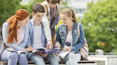 Four students sitting on a bench reading a document