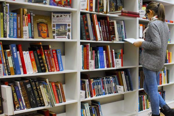 Female student stands reading book in front of bookshelves in college library