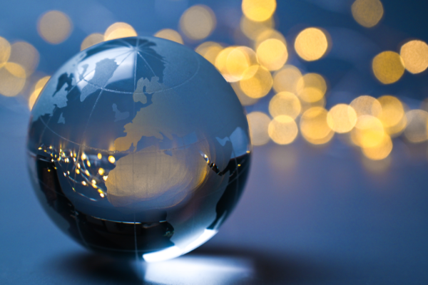A glass globe sits on a dark grey surface; in the distance, out of focus lights glimmer; these are reflected as pinpricks of light within the glass globe.