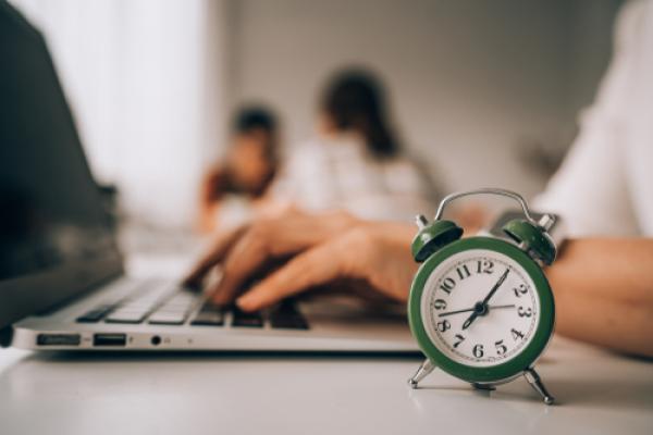 Hands typing on a laptop with small green alarm clock in foreground, indicating time pressure