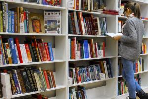 Female student stands reading book in front of bookshelves in college library