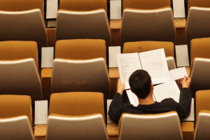 Rear view of man seated in empty lecture hall examining printed documents
